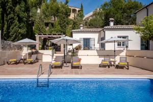a pool with chairs and umbrellas next to a house at Villa Atréju in Cómpeta