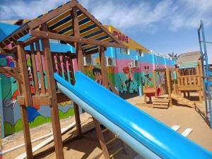 a playground with a blue slide in front of a mural at Halaشاليه in Ras Sedr