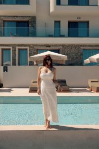 a woman in a white dress standing next to a swimming pool at La Brise Luxury Suites in Nea Peramos