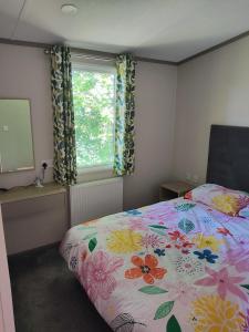 a bedroom with a bed with a floral comforter and a window at Rosie Caravan Selsey in Selsey