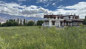 a large house in a field with mountains in the background at Cho Farm House in Leh