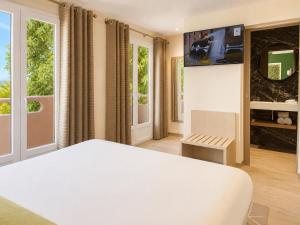 a bedroom with a white bed and a tv at Hôtel Le Mistral in Porto-Vecchio