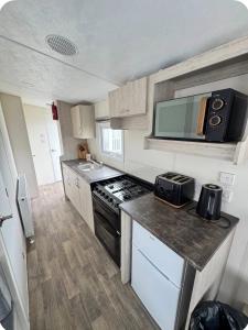 a small kitchen with a stove and a microwave at Brand New Caravan in Selsey +5 photos