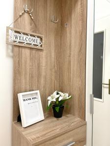 a welcome sign on a wooden door with a plant on a shelf at Apartman LUXE STAY Vujović in Bileća +1 photo