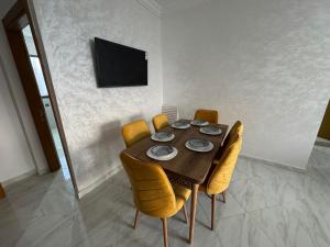 a dining room table with yellow chairs and a television at Al Hoceima - Vue sur la mer- Green Village Trougout in Al Hoceïma