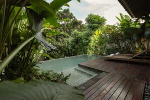 a pool in a garden with a wooden deck at Apittoya Villas in Gianyar
