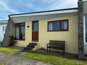a bench sitting outside of a yellow house at Bungalow 19 Widemouth Bay in Poundstock