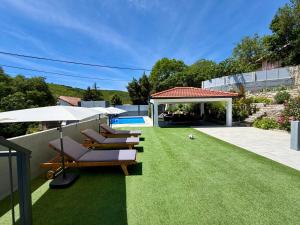 a lawn with lounge chairs and an umbrella and a pool at Kameni dvori - Family Villa with Pool & Jacuzzi for 8 in Imotski