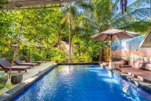 a pool with chairs and an umbrella and trees at Ortigia Tropical Lodge in Gili Trawangan
