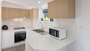 a white kitchen with a microwave and a sink at Aqua Breeze by Experience Jervis Bay in Vincentia