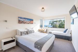a bedroom with a bed and a couch and a window at Bay View Escape in Binalong Bay