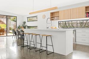 a kitchen with a white counter and stools at Tea Tree Poolside Escape in Inverloch