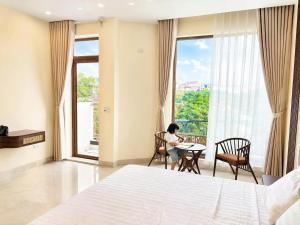 a woman sitting at a table in a bedroom with a window at O Lily Hotel in Ninh Binh
