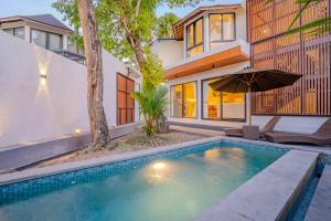 a swimming pool with an umbrella in front of a house at Sanara Oasis Villa in Canggu