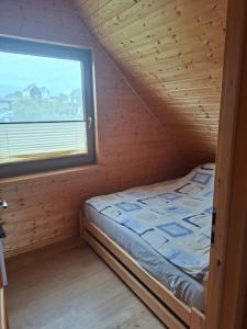 a bed in a wooden room with a window at Całoroczny dom letniskowy in Chmielno