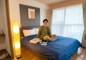 a man sitting on a bed in a bedroom at 札幌駅近 すすきの中心部 スーペリアルーム最大7名 家族やグループにお勧め 市電駅前 北海道観光食事最高立地 11歳まで子供無料 高級ベッドマットレス使用 チェックアウト11時 in Sapporo