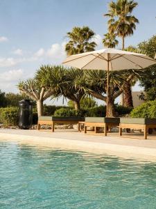 two benches and an umbrella next to a swimming pool at Casa da Ria in Tavira
