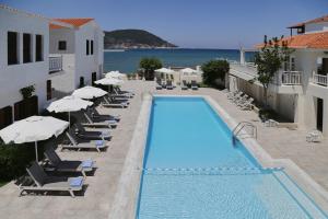 a swimming pool with chairs and umbrellas and the ocean at Skopelos Village Hotel in Skopelos Town