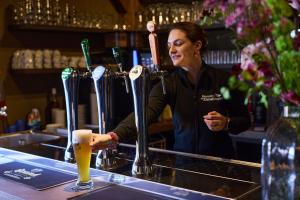 a woman standing behind a bar with a glass of beer at Kampeerdorp de Zandstuve - Kindvriendelijke Vakantiepark in Rheeze +8 photos