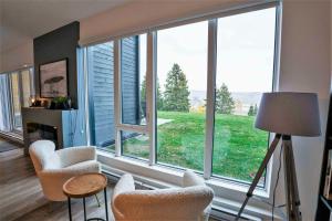 a living room with a large window with chairs and a table at Terrace Condo with River View and Pool in Baie-Saint-Paul
