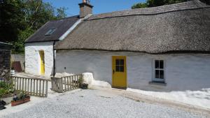 a white cottage with a thatched roof with a yellow door at The Thatched Cottage in Cork +25 photos