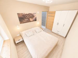a white bedroom with a bed and a window at Zója Apartmanház in Nagykanizsa