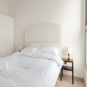 a white bedroom with a large white bed and a side table at Sea View Tower - 33rd Floor l Parking l Mamad in Bat Yam