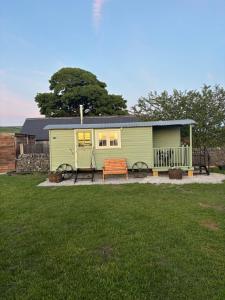 a green tiny house with a bench in a yard at Shepherds Rest in Peak Forest
