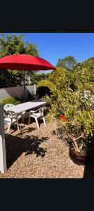 a picnic table with a red umbrella next to a bush at Appartement causy in Gonfreville-lʼOrcher