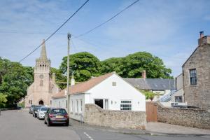 a small white building with a church in the background at Northern Hideaways, Iona Cottage in Newcastle upon Tyne