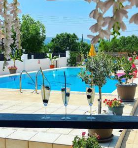 three wine glasses sitting on a table near a swimming pool at Lecini Studios with Pool, by ZanteWize in Laganas