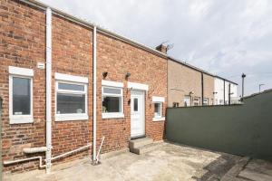 a brick building with a white door and a green fence at Spacious Beach House Near Promenade & Beach Sleeps 6 in Newbiggin-by-the-Sea