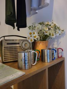 three metal mugs sitting on top of a table with flowers at Pajtl indoor glamping in Črna na Koroškem
