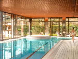 a woman walks by a pool in a house at Millennium Hotel Paris Charles De Gaulle in Roissy-en-France