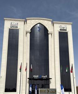 a building with glass windows and flags in front of it at إليت الجامعة -Elite Served Apartments - Hafar Al-Batin in Hafr Al-Batin