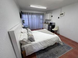 a bedroom with a white bed and a kitchen at Protea Hoogte Flatlet in Brackenfell