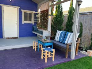 a porch with a couch and a table and stools at פרא בקתות אירוח - מתחם נופש כפרי עם בריכה פרטית in Nir Yafe