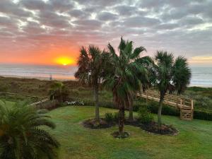 a sunset over a beach with two palm trees at Moss Landing Luxury Beachfront Private Walkover in Bolivar Peninsula +29 photos