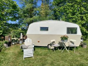 a white caravan parked in the grass with chairs and a table at The running Rabbit caravan in Ystad