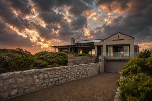a house with a stone wall and a cloudy sky at Peninsula Villa - Romansbaai in Gansbaai