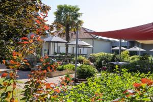 a patio with tables and umbrellas in a garden at The Originals City, Le Patio Hôtel, Cholet Nord in Beaupréau