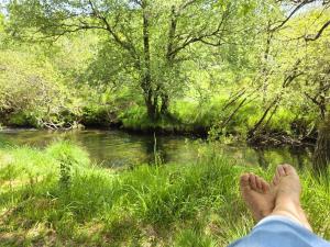 a persons feet in the grass next to a river at Moinhos do Poço Verde in Castro Laboreiro