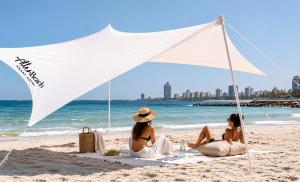 two women sitting on the beach under a white tent at Allenbeach TLV- Adults only - WE HAVE SHELTER in Tel Aviv