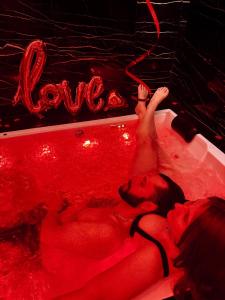 a woman laying in a bathtub covered in red lights at 007 Loveroom Secrète Jacuzzi privé Cinéma 4K in Courcouronnes