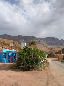 a dirt road with a blue building and mountains in the background at La Auberge Gite Rural Tatiouine Midelt in Tattiouine