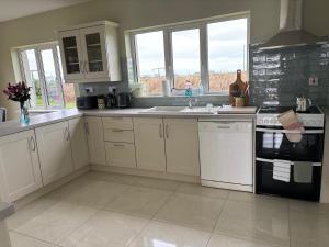 a kitchen with white cabinets and a sink and windows at Beach view Bungalow in Spanish Point
