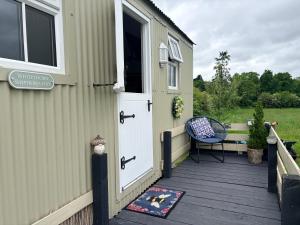 a green house with a door and a chair on a deck at Whitethorn Shepherds Hut in Bellaghy +12 photos