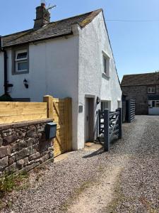 a white house with a wooden gate and a stone wall at Charming cosy cottage near the Lake District in Penrith