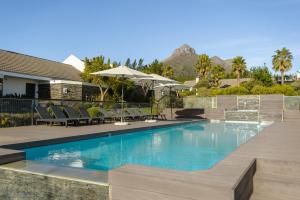 a pool with chairs and umbrellas next to a house at Stellenbosch Luxury Apartments in Stellenbosch