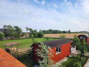 a red house with a black roof in a field at Herdershut 'Het Schoehuis', vlakbij zee in Sint Maartensbrug